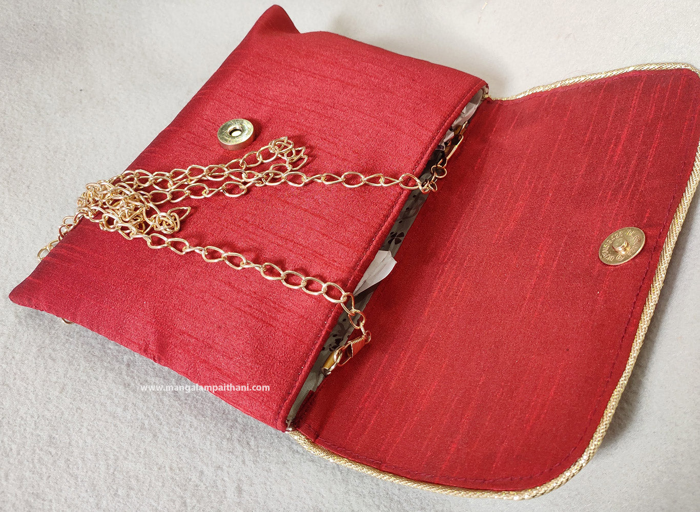 A pink clutch purse with a floral design and a gold chain strap.
