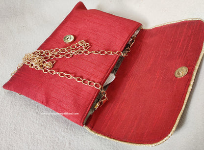 A pink clutch purse with a floral design and a gold chain strap.