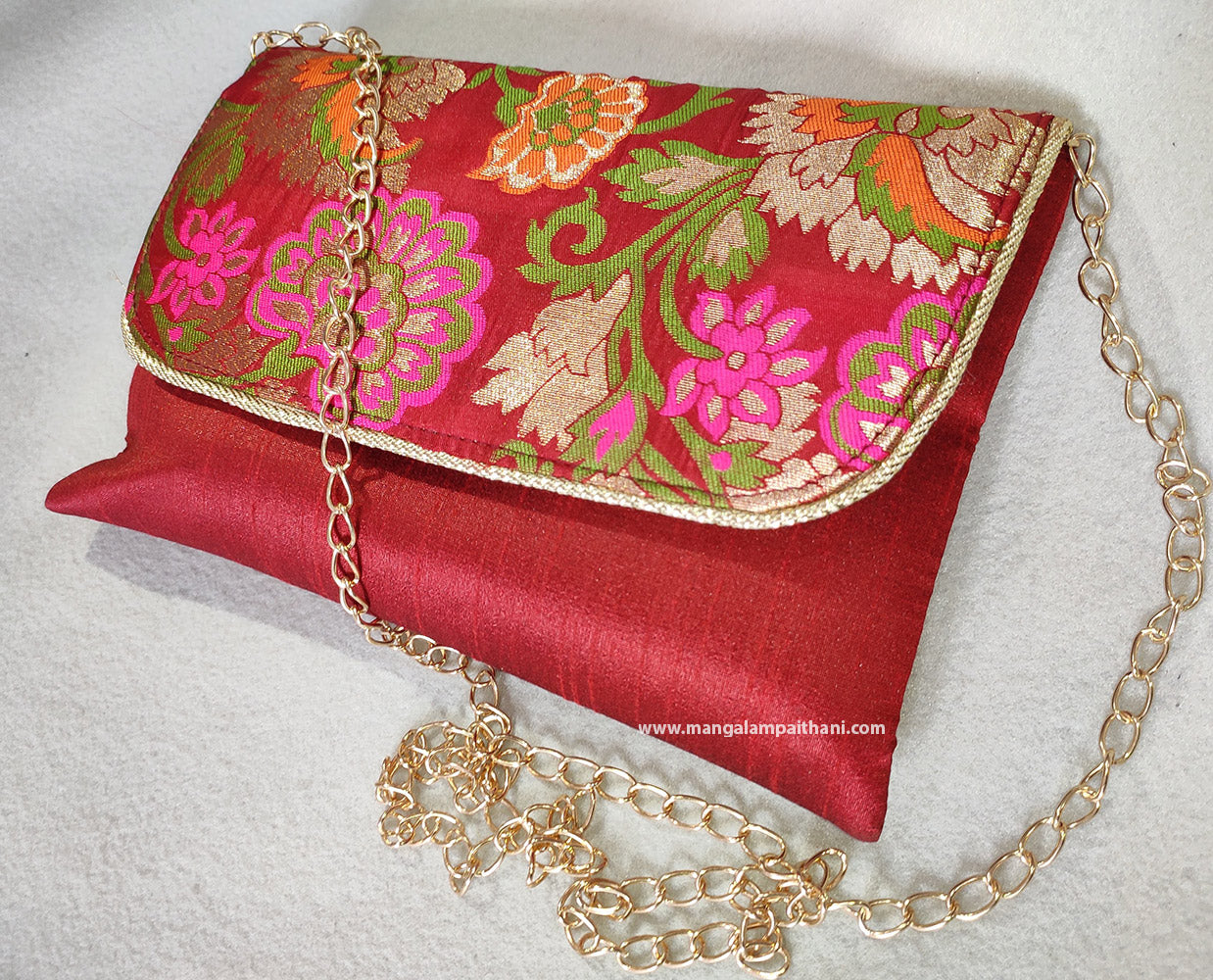 A pink clutch purse with a floral design and a gold chain strap.