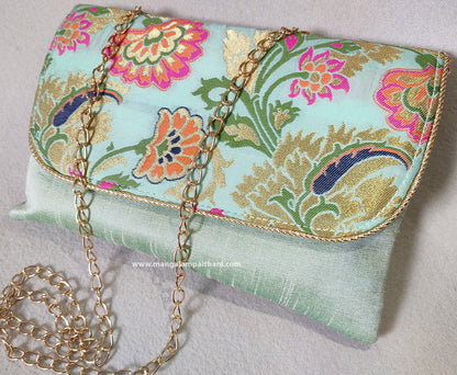 A blue clutch purse with a floral design and a detachable gold chain strap.
