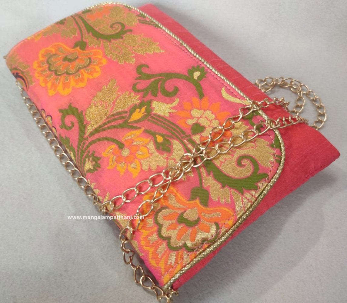 A pink clutch purse with a floral design and a gold chain strap.